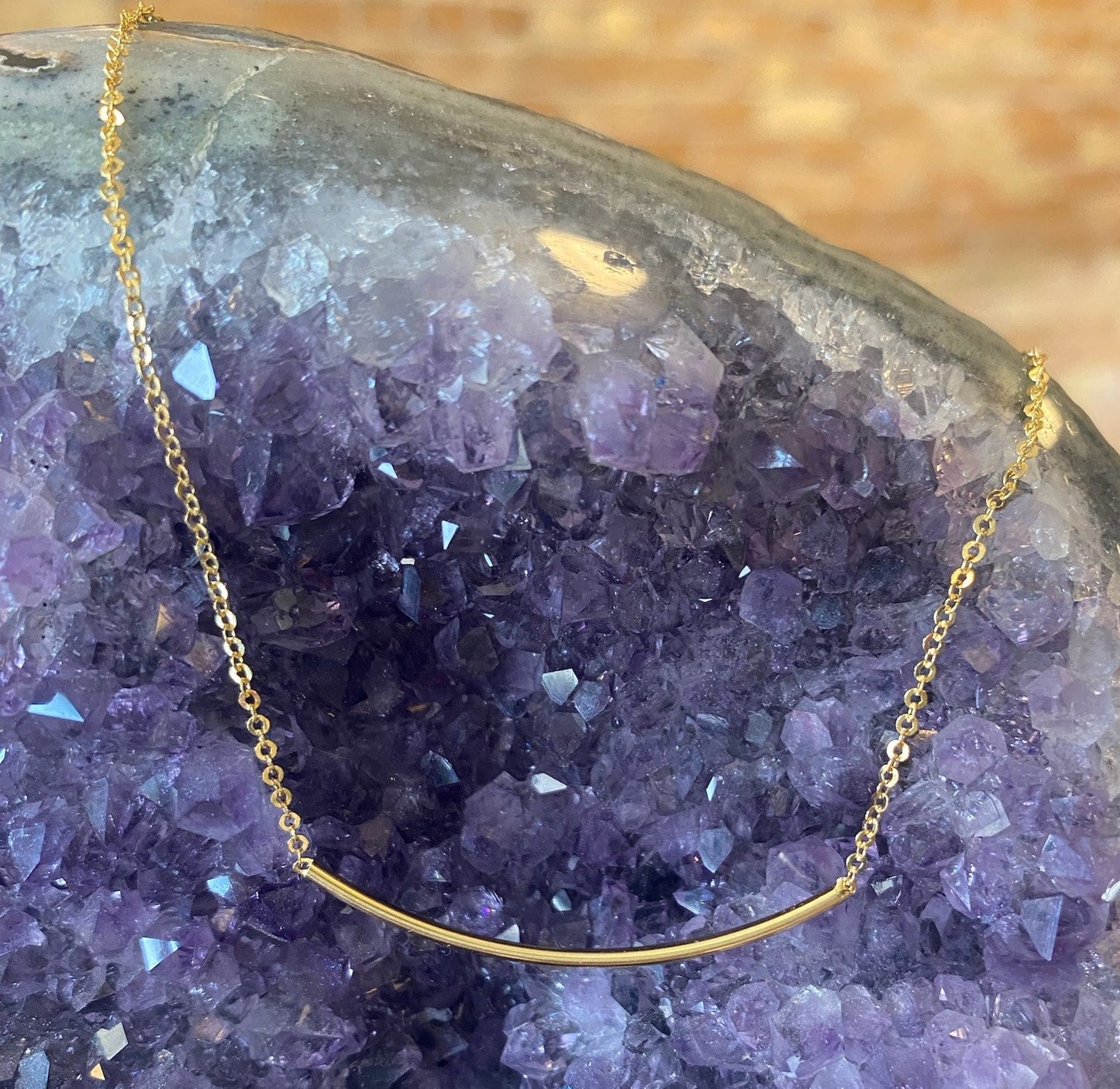 Photo of 14 Karat Yellow Gold Smile Curved Necklace in a decorative scene, designed by , available at Plumb Gold & Plumb Silver