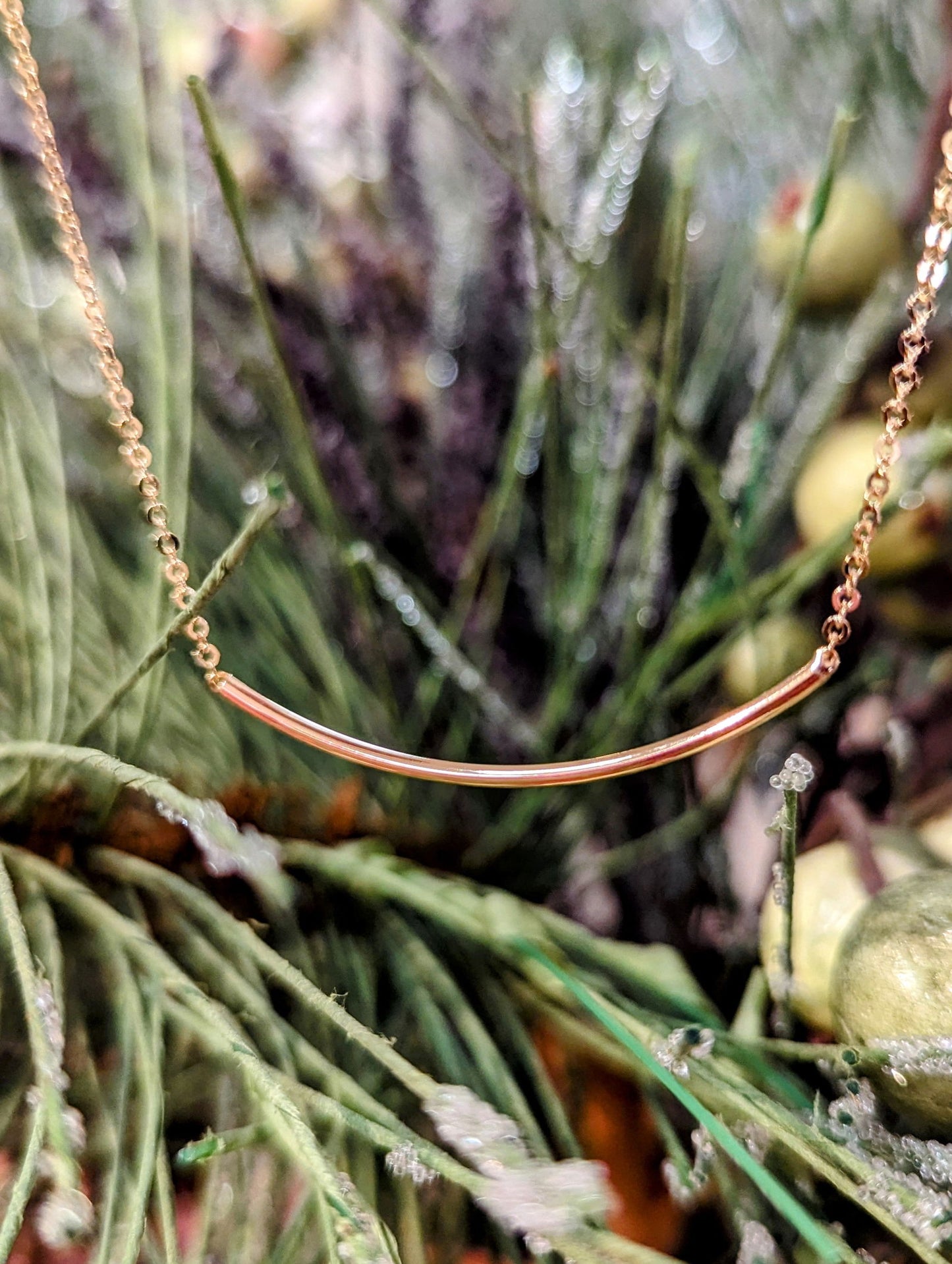 Photo of 14 Karat Yellow Gold Smile Curved Necklace in a decorative scene, designed by , available at Plumb Gold & Plumb Silver