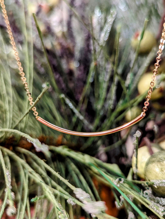 Photo of 14 Karat Yellow Gold Smile Curved Necklace in a decorative scene, designed by , available at Plumb Gold & Plumb Silver