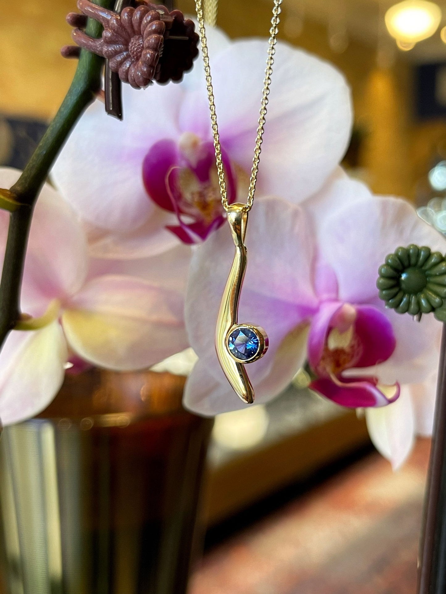 Photo of Blue Sapphire Curve Pendant in a decorative scene, designed by , available at Plumb Gold & Plumb Silver