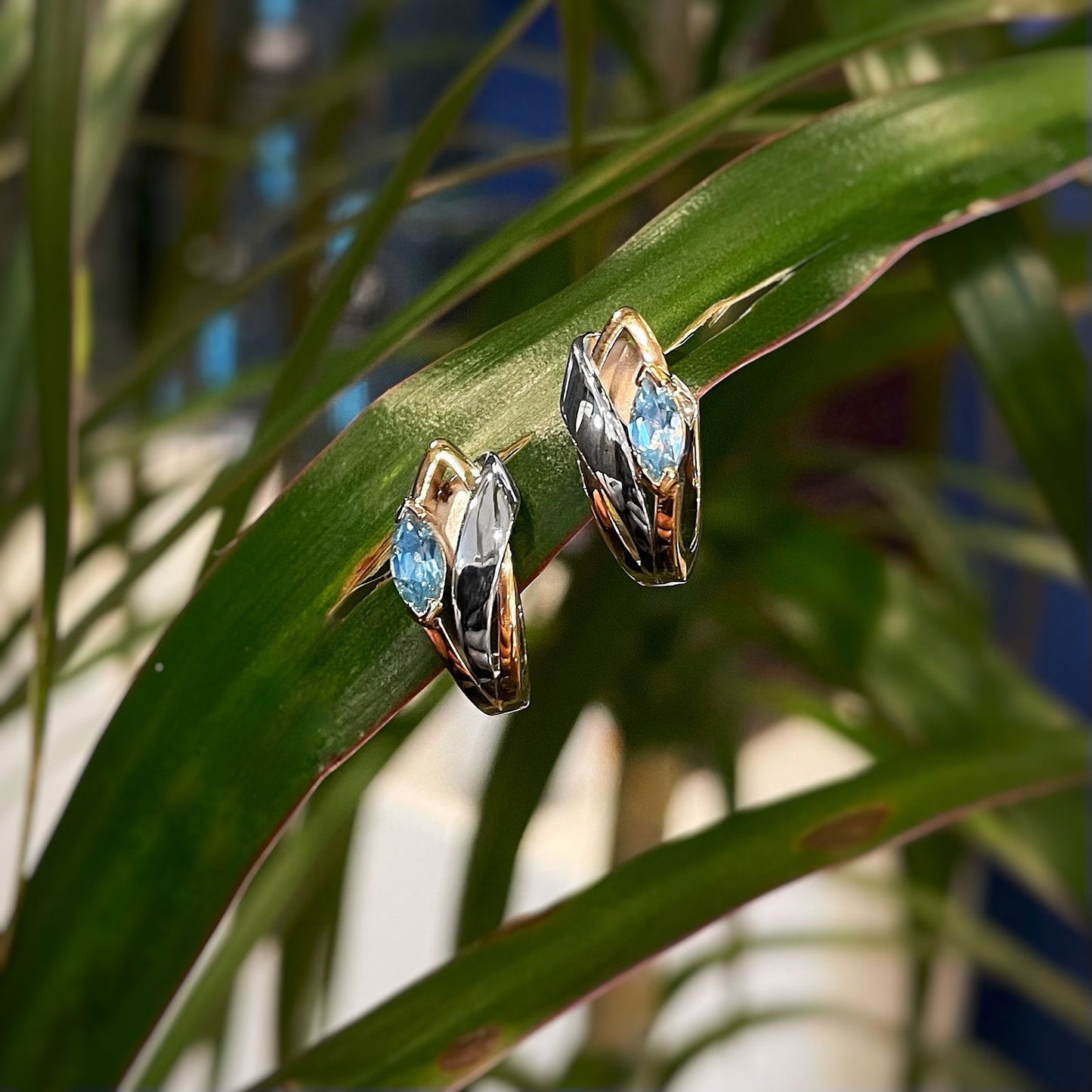 Photo of Blue Topaz Marquise Huggies in a decorative scene, designed by , available at Plumb Gold & Plumb Silver