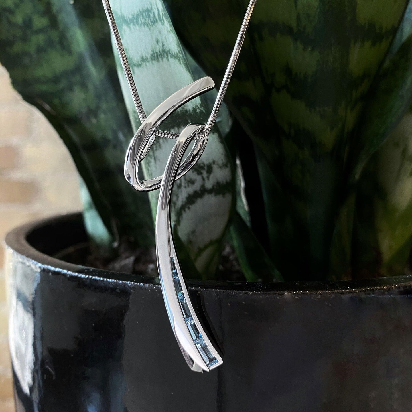 Photo of Blue Topaz Swoop Pendant in a decorative scene, designed by , available at Plumb Gold & Plumb Silver
