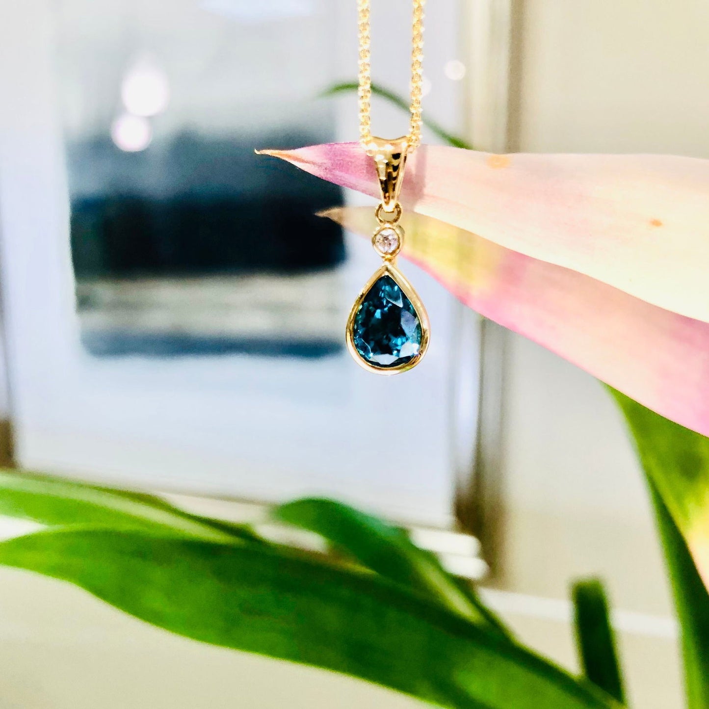 Photo of Blue Zircon Diamond Drop Pendant in a decorative scene, designed by , available at Plumb Gold & Plumb Silver