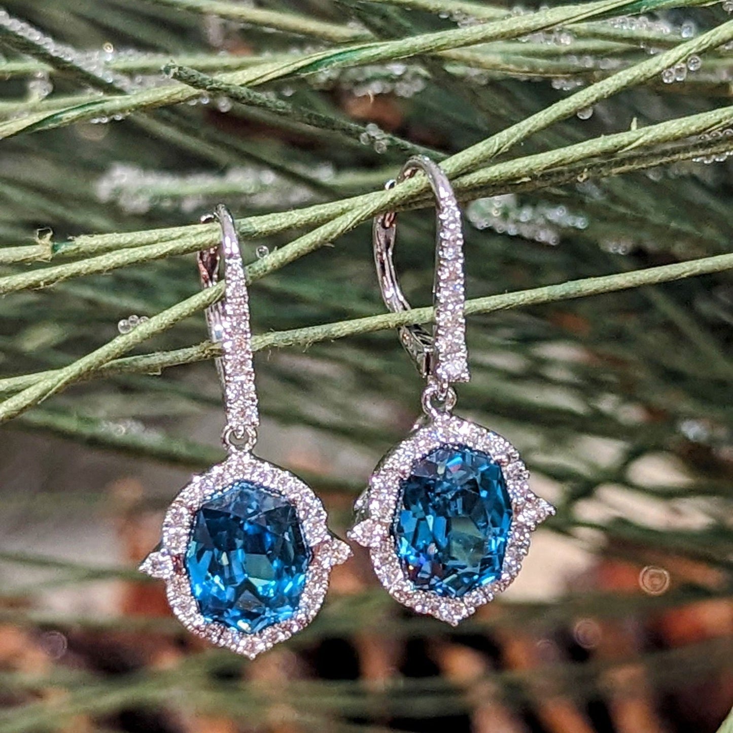 Photo of Blue Zircon Halo Dangle Earrings in a decorative scene, designed by , available at Plumb Gold & Plumb Silver