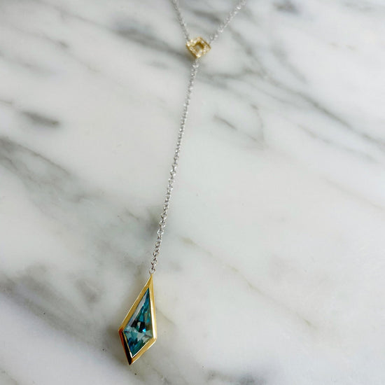 Photo of Blue Zircon Kite "Y" Necklace in a decorative scene, designed by , available at Plumb Gold & Plumb Silver