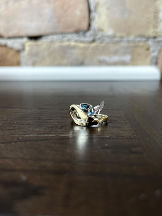 Photo of Breuning Blue Topaz Swoop Ring in a decorative scene, designed by , available at Plumb Gold & Plumb Silver