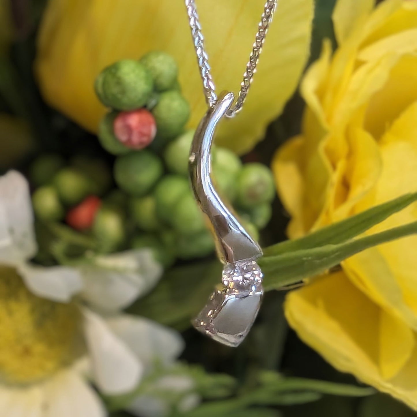 Photo of Curve Diamond Pendant in a decorative scene, designed by , available at Plumb Gold & Plumb Silver