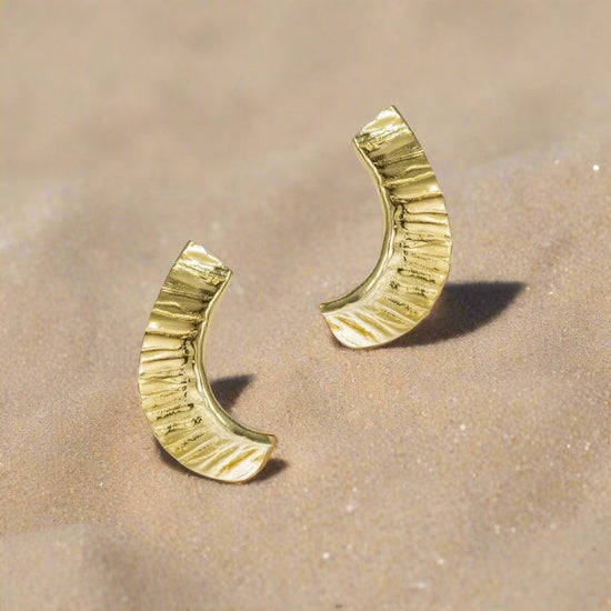 Photo of Curved Seaweed Earring in a decorative scene, designed by -, available at Plumb Gold & Plumb Silver