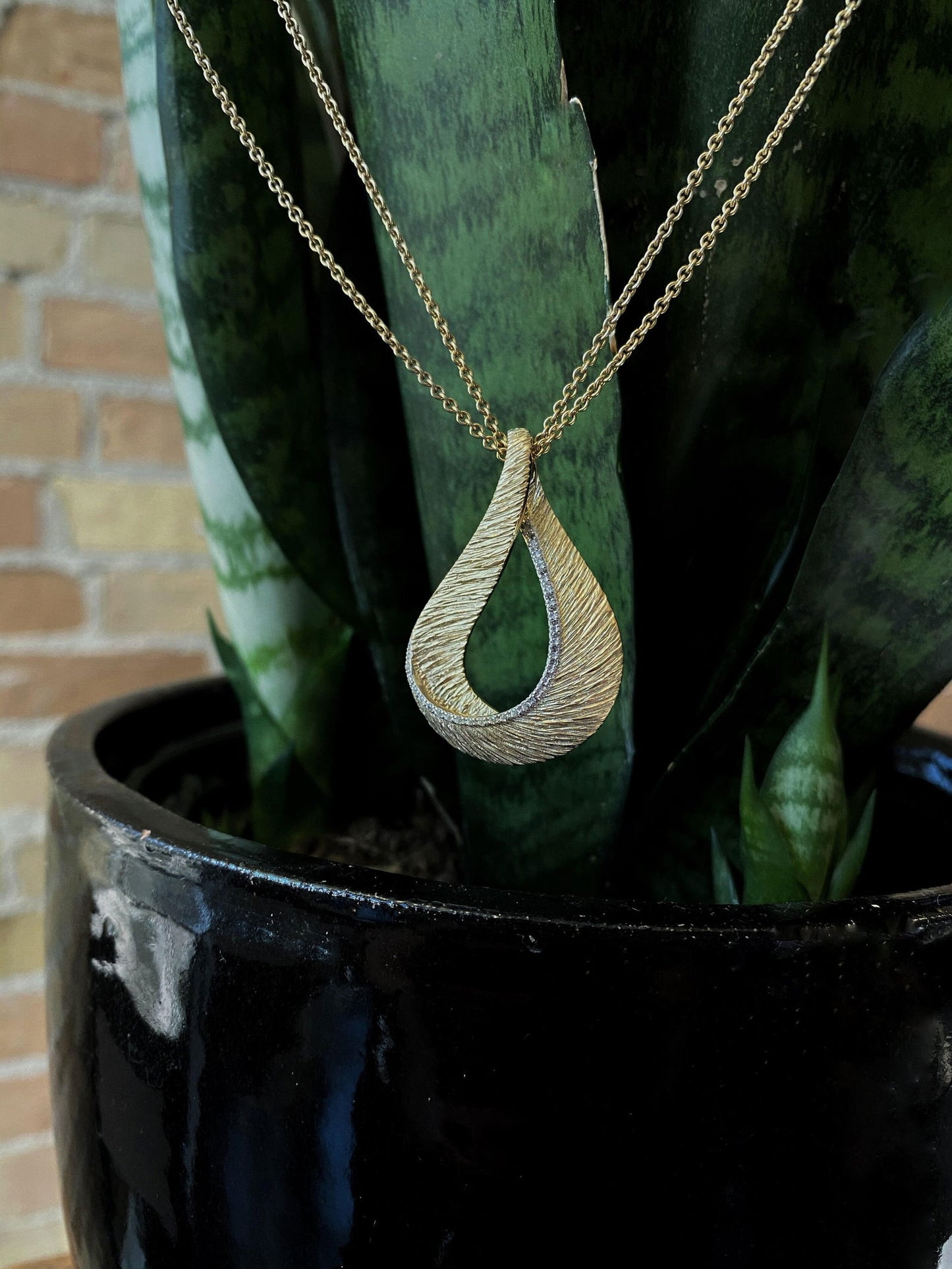 Photo of Diamond Cut Loop Pendant with White Sapphire Accents in a decorative scene, designed by , available at Plumb Gold & Plumb Silver