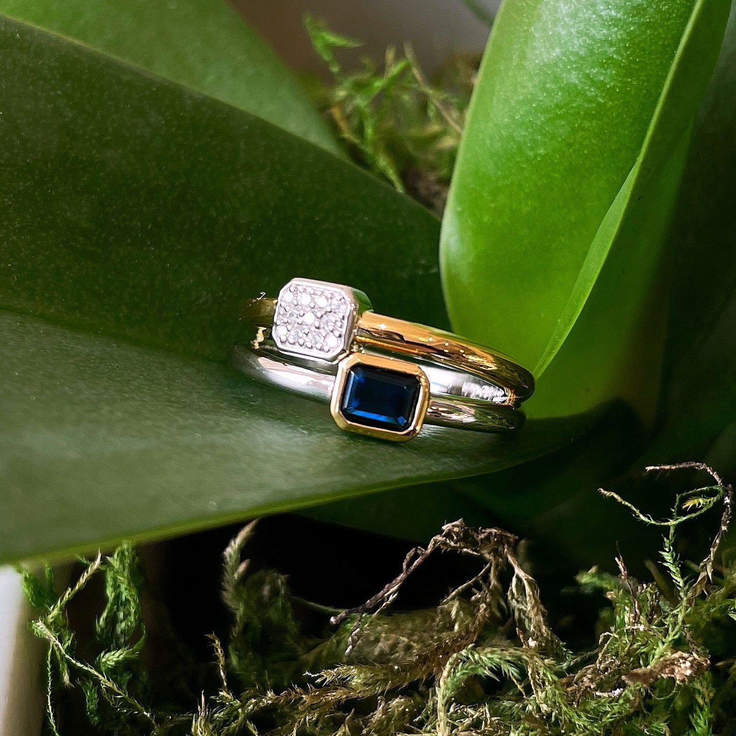 Photo of "Duo" Blue Bezel CZ Cluster Ring in a decorative scene, designed by , available at Plumb Gold & Plumb Silver