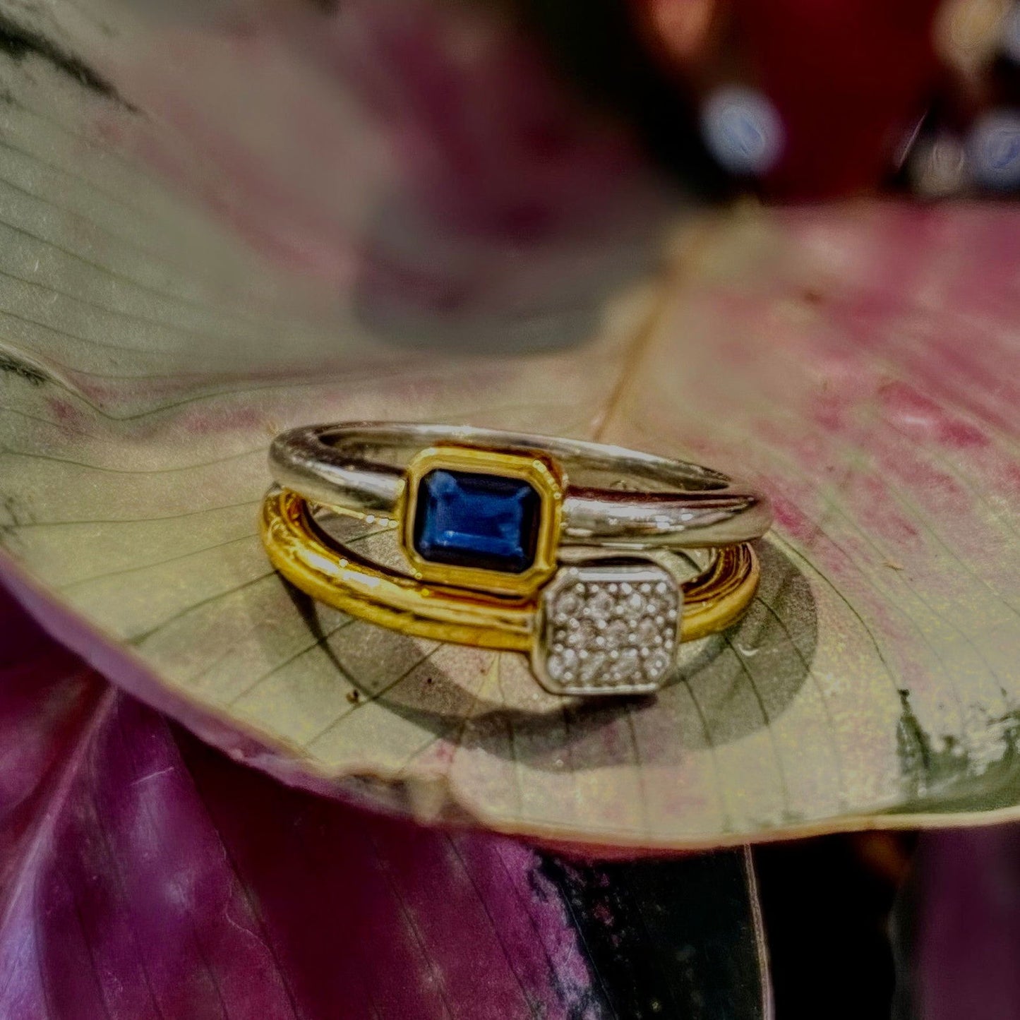 Photo of "Duo" Blue Bezel CZ Cluster Ring in a decorative scene, designed by , available at Plumb Gold & Plumb Silver