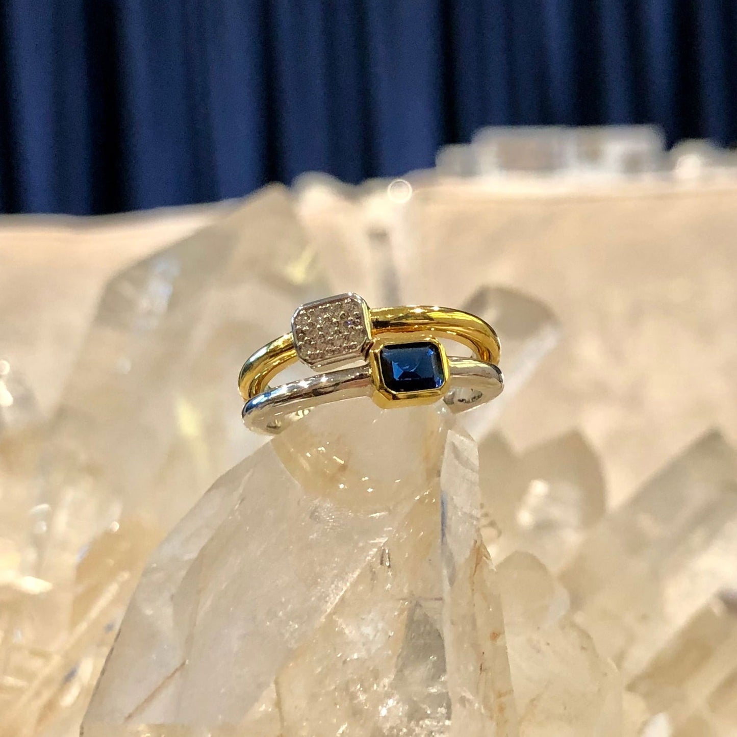Photo of "Duo" Blue Bezel CZ Cluster Ring in a decorative scene, designed by , available at Plumb Gold & Plumb Silver