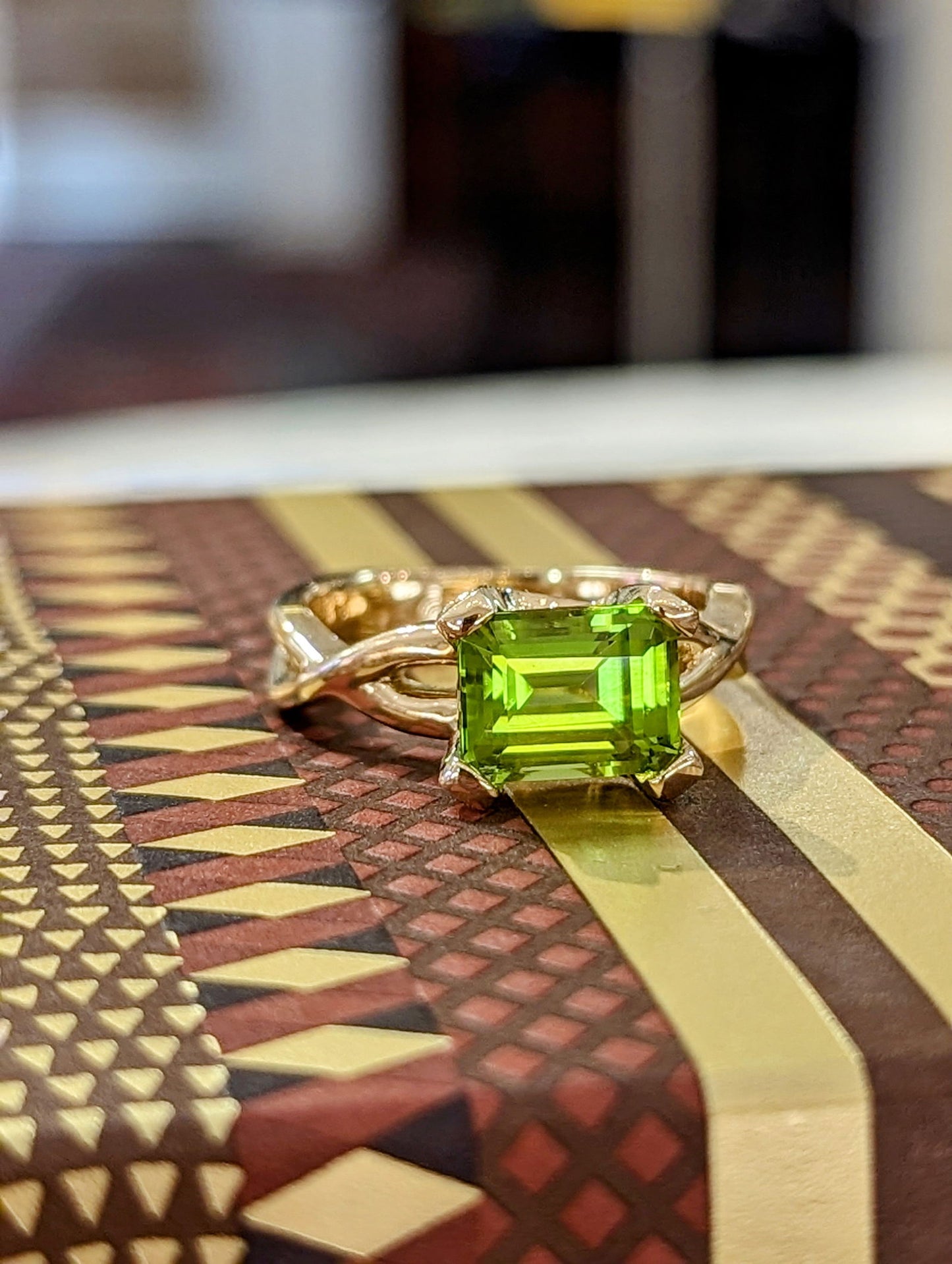 Photo of Emerald Cut Peridot Twisted Shank Ring in a decorative scene, designed by , available at Plumb Gold & Plumb Silver