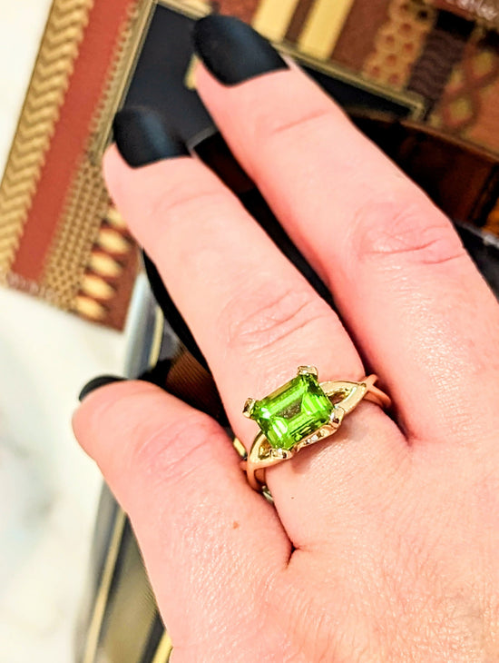 Photo of Emerald Cut Peridot Twisted Shank Ring in a decorative scene, designed by , available at Plumb Gold & Plumb Silver