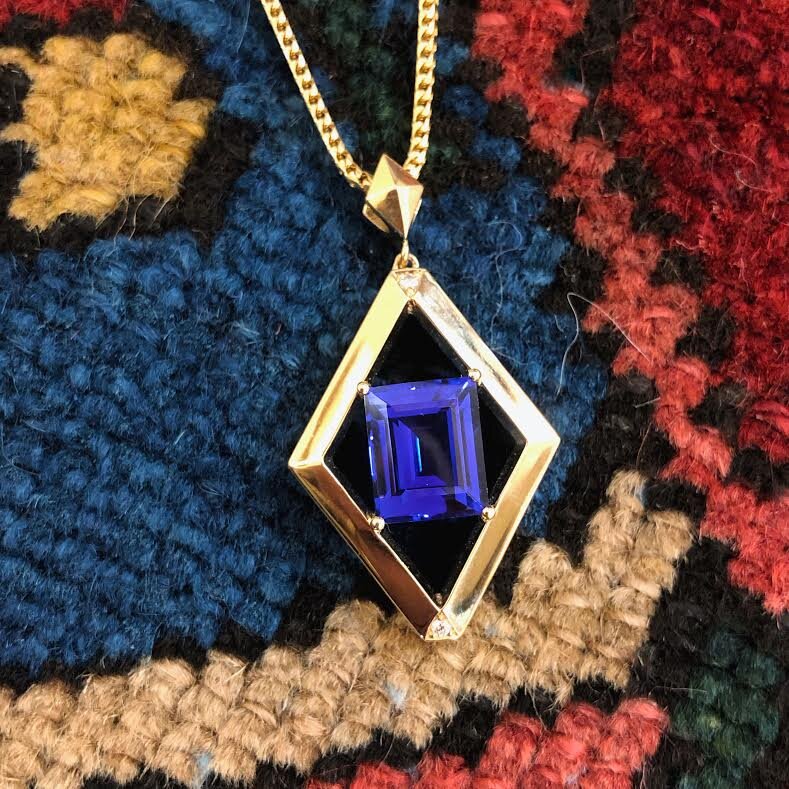 Photo of Emerald Cut Tanzanite Pendant in a decorative scene, designed by , available at Plumb Gold & Plumb Silver