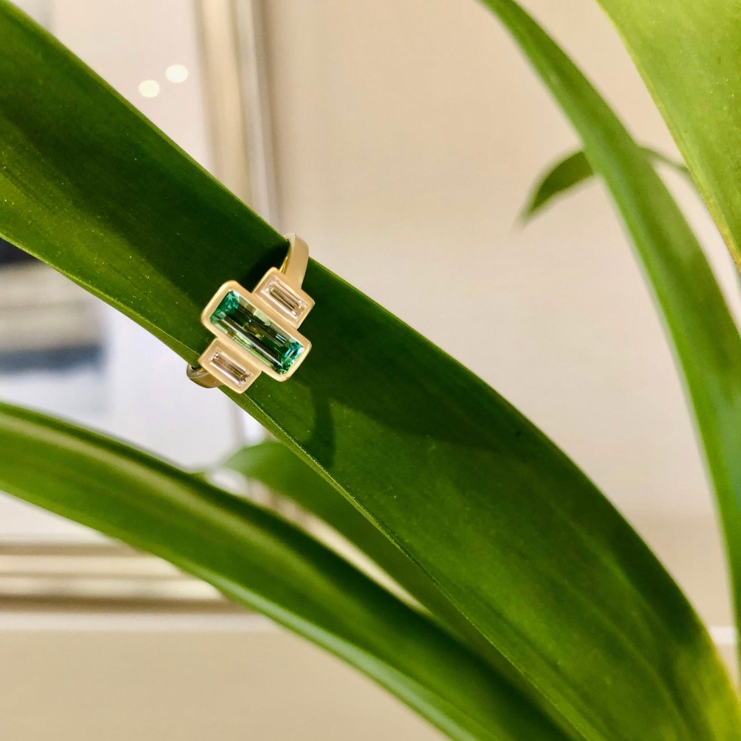 Photo of Emerald & Diamond Baguette Satin Ring in a decorative scene, designed by , available at Plumb Gold & Plumb Silver