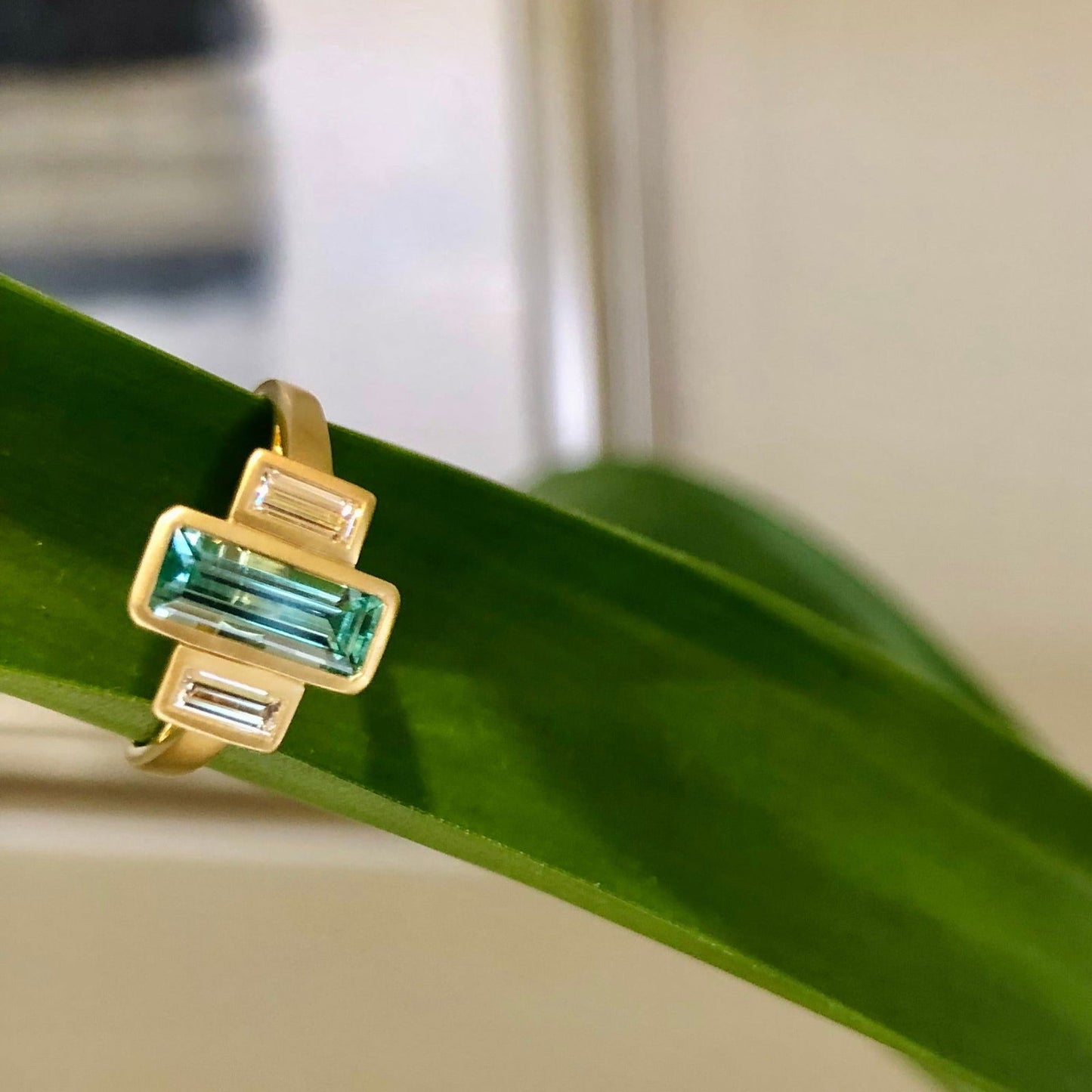 Photo of Emerald & Diamond Baguette Satin Ring in a decorative scene, designed by , available at Plumb Gold & Plumb Silver