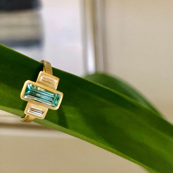 Photo of Emerald & Diamond Baguette Satin Ring in a decorative scene, designed by , available at Plumb Gold & Plumb Silver