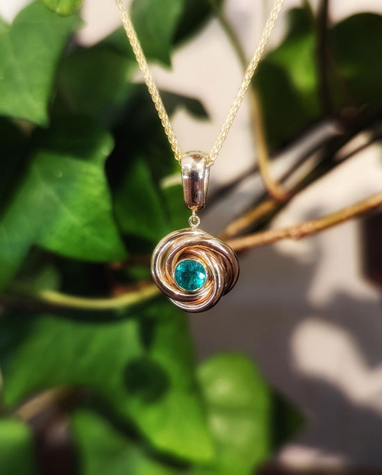 Photo of Emerald Love Knot Pendant in a decorative scene, designed by , available at Plumb Gold & Plumb Silver
