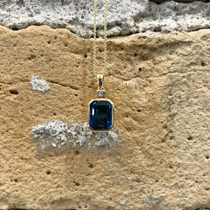 Photo of Emerald Octagon-Cut London Blue Topaz Bezel Pendant in a decorative scene, designed by , available at Plumb Gold & Plumb Silver