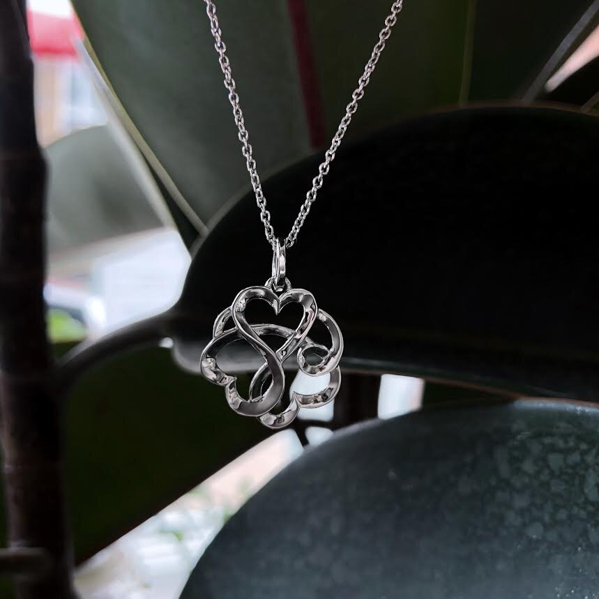 Photo of Entwined Hearts Necklace in a decorative scene, designed by , available at Plumb Gold & Plumb Silver