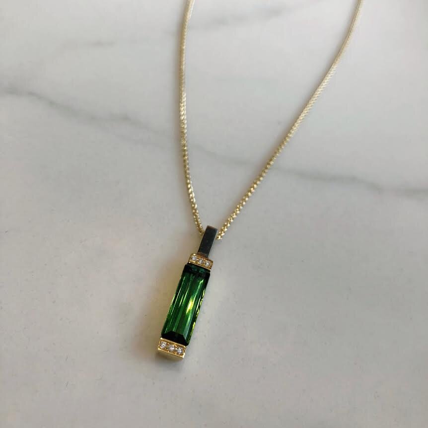 Photo of Green Tourmaline and Diamond Bar Pendant in a decorative scene, designed by , available at Plumb Gold & Plumb Silver