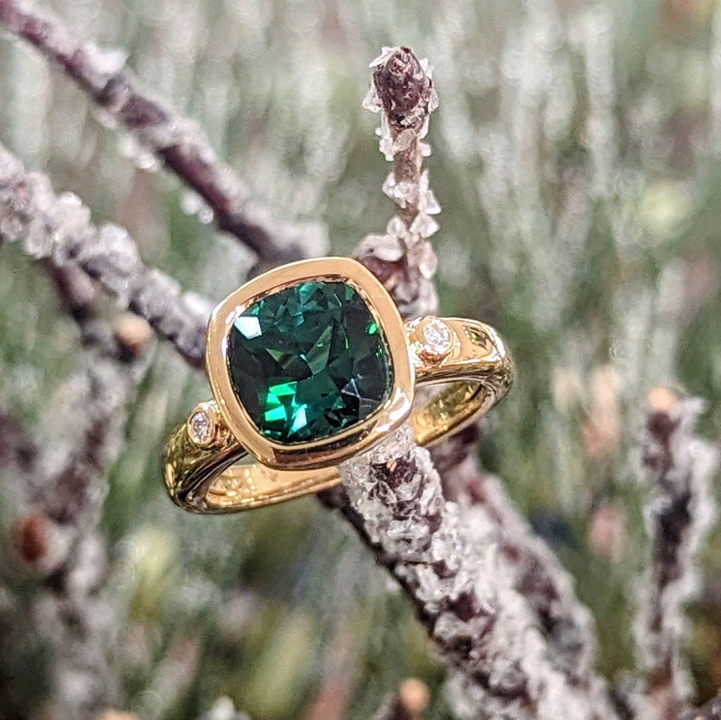 Photo of Green Tourmaline cushion Bezel Ring in a decorative scene, designed by , available at Plumb Gold & Plumb Silver