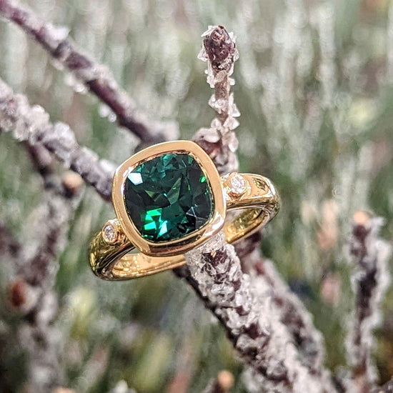 Photo of Green Tourmaline cushion Bezel Ring in a decorative scene, designed by , available at Plumb Gold & Plumb Silver