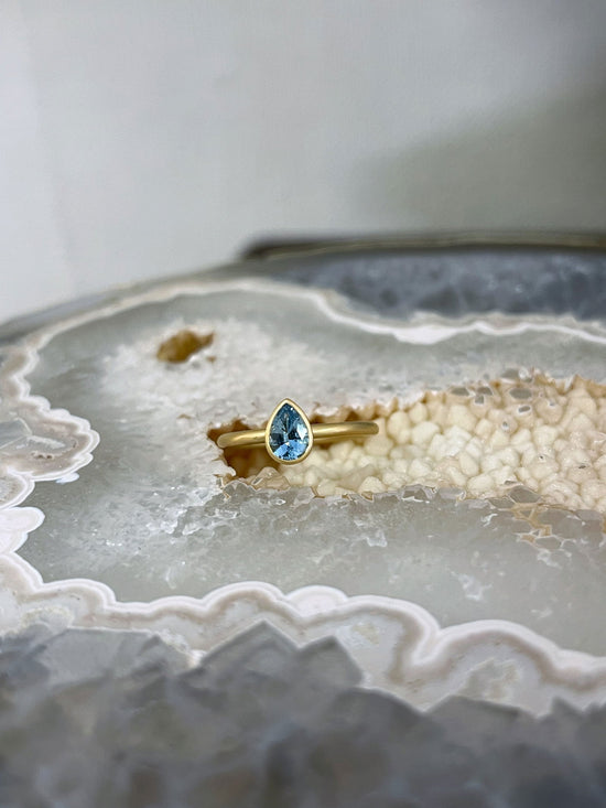 Photo of Kim Collins Aquamarine Yumdrop in a decorative scene, designed by , available at Plumb Gold & Plumb Silver