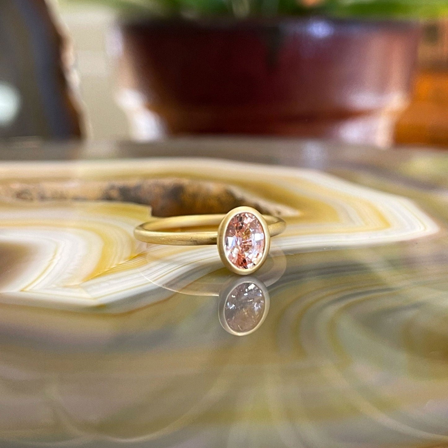 Photo of Kim Collins Peach Sapphire Yumdrop Ring in a decorative scene, designed by , available at Plumb Gold & Plumb Silver