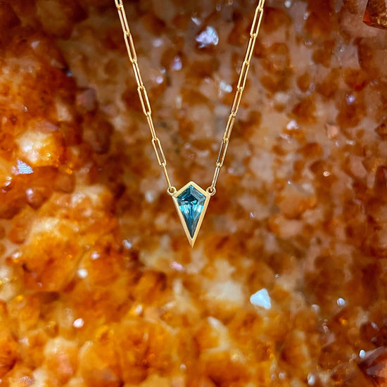 Photo of Kimberly Collins Blue Zircon Kite Necklace in a decorative scene, designed by , available at Plumb Gold & Plumb Silver