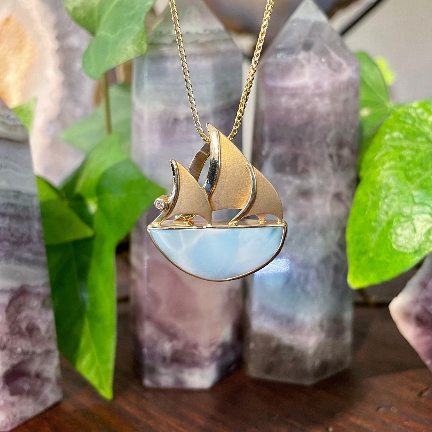 Photo of Larimar Sailboat Pendant in a decorative scene, designed by , available at Plumb Gold & Plumb Silver