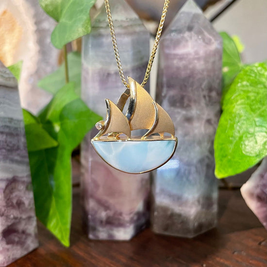 Photo of Larimar Sailboat Pendant in a decorative scene, designed by , available at Plumb Gold & Plumb Silver