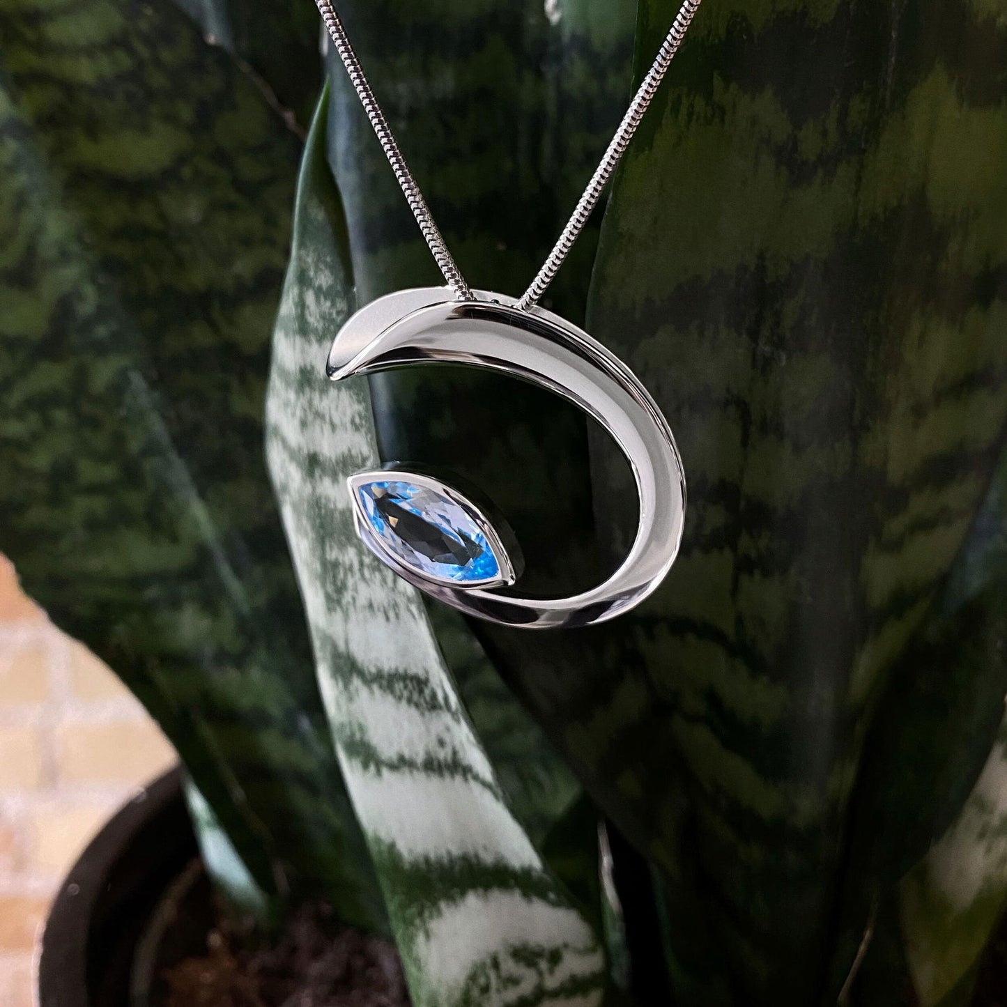 Photo of Marquise Blue Topaz "C" Pendant in a decorative scene, designed by , available at Plumb Gold & Plumb Silver