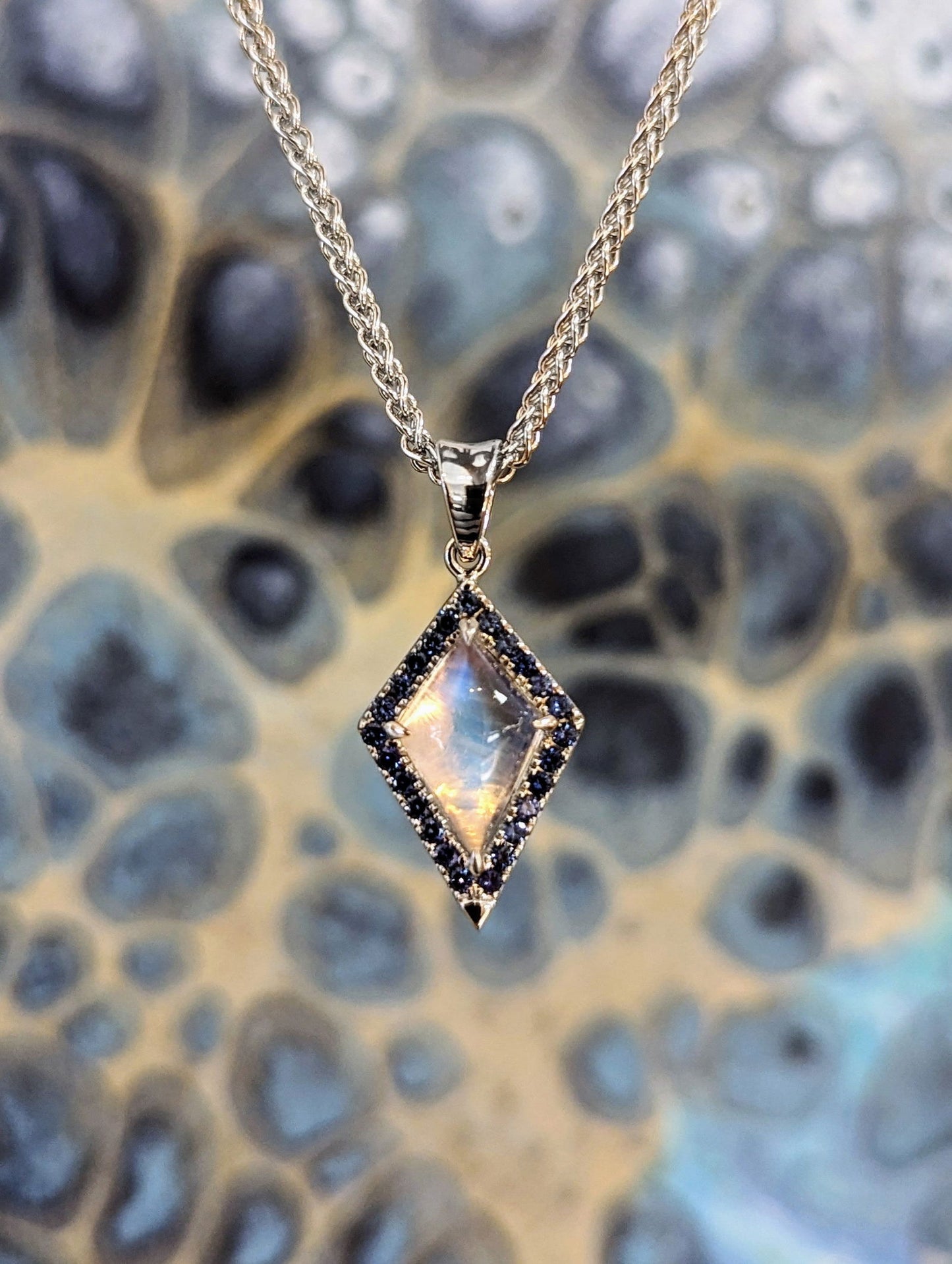 Photo of Moonstone and Sapphire Pendant in a decorative scene, designed by , available at Plumb Gold & Plumb Silver