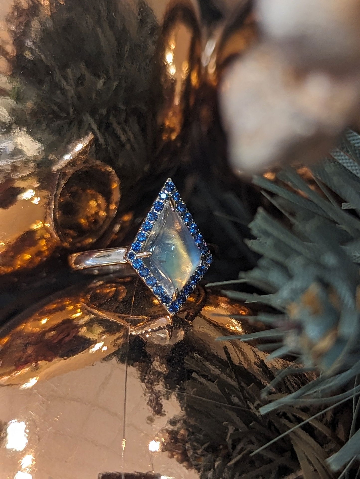Photo of Moonstone and Sapphire Ring in a decorative scene, designed by , available at Plumb Gold & Plumb Silver