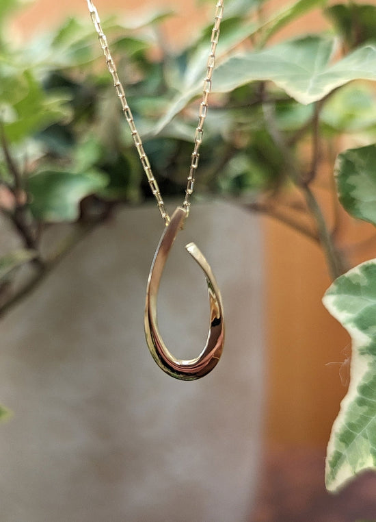 Photo of Open Teardrop Necklace in a decorative scene, designed by , available at Plumb Gold & Plumb Silver