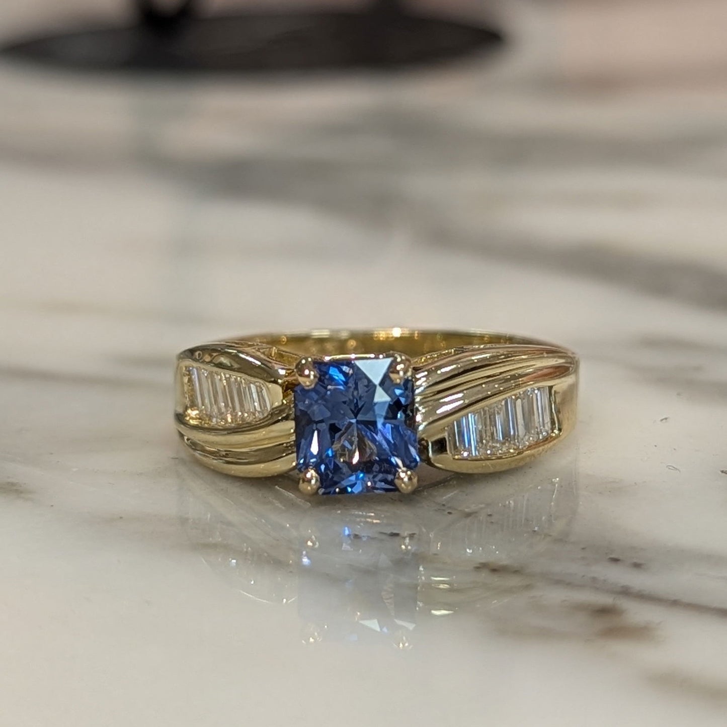 Photo of Radiant Sapphire and Baguette Ring in a decorative scene, designed by , available at Plumb Gold & Plumb Silver
