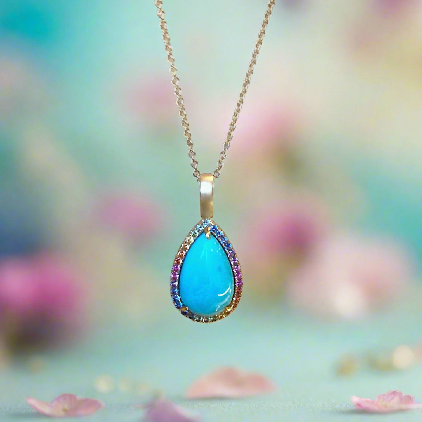 Photo of Rainbow Sapphire Halo Turquoise Pendant in a decorative scene, designed by , available at Plumb Gold & Plumb Silver