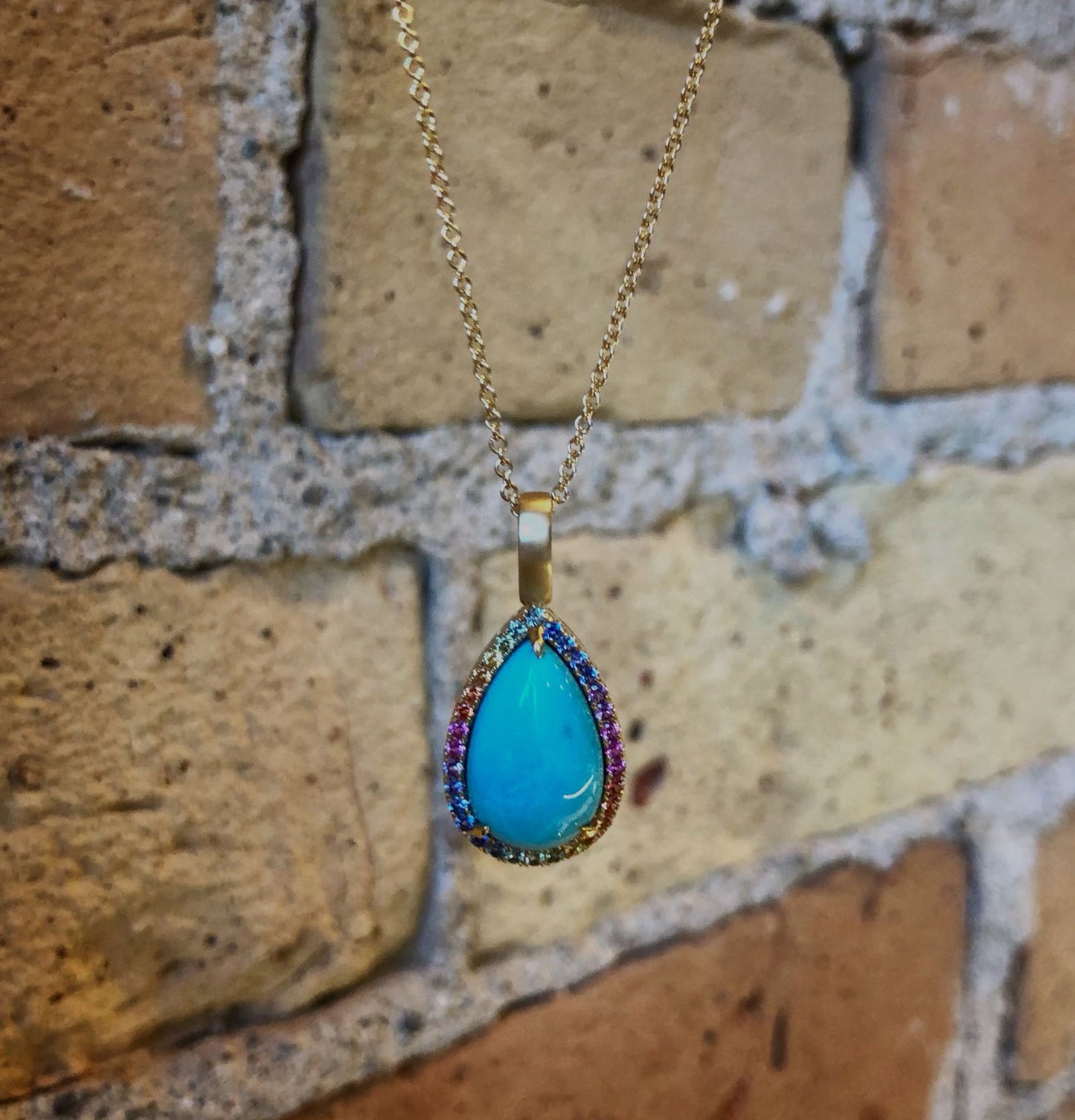 Photo of Rainbow Sapphire Halo Turquoise Pendant in a decorative scene, designed by , available at Plumb Gold & Plumb Silver
