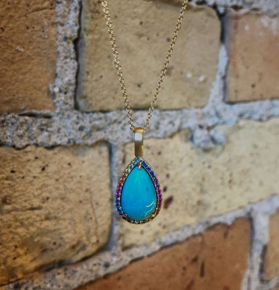 Photo of Rainbow Sapphire Halo Turquoise Pendant in a decorative scene, designed by , available at Plumb Gold & Plumb Silver