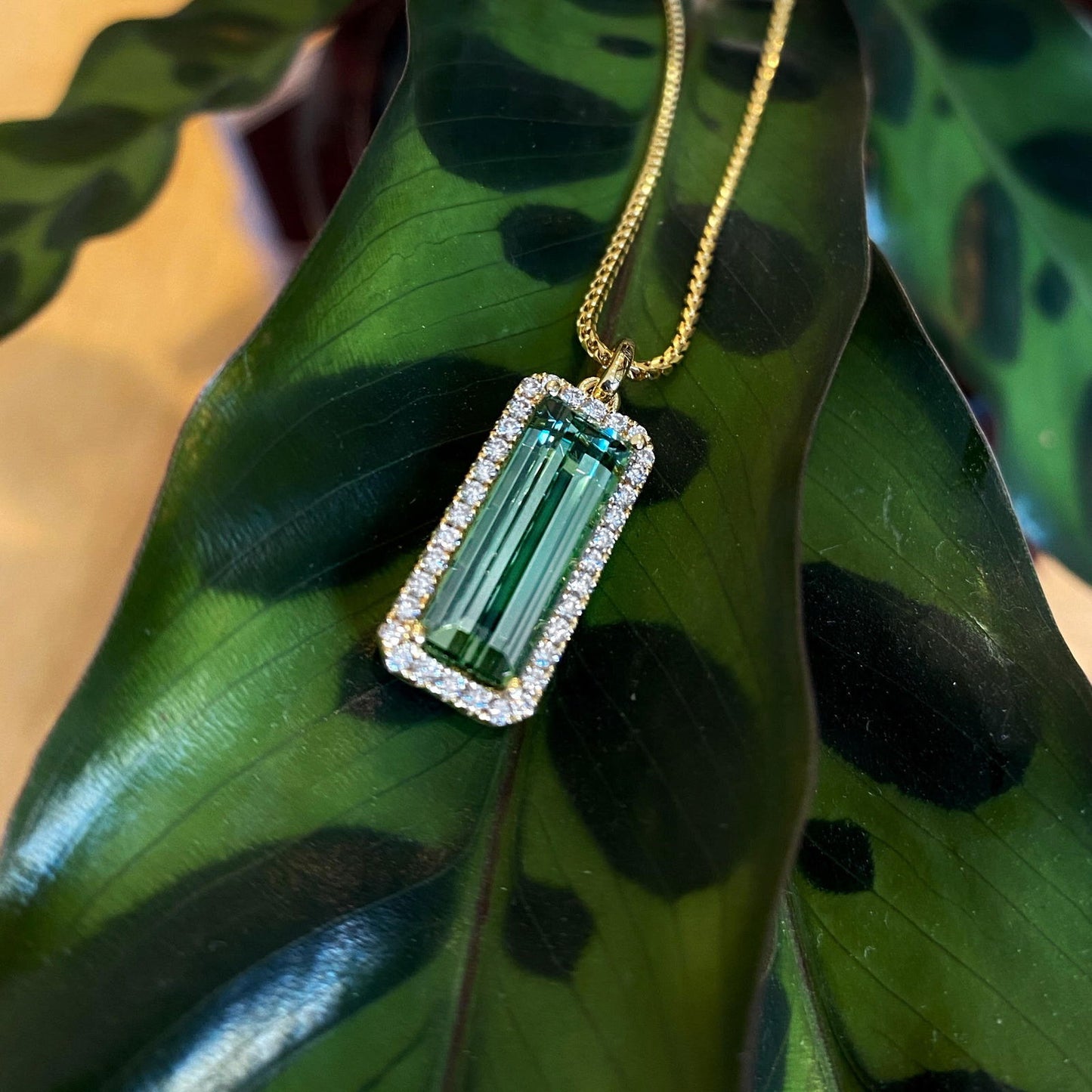 Photo of Rectangle Tourmaline Halo Pendant in a decorative scene, designed by , available at Plumb Gold & Plumb Silver