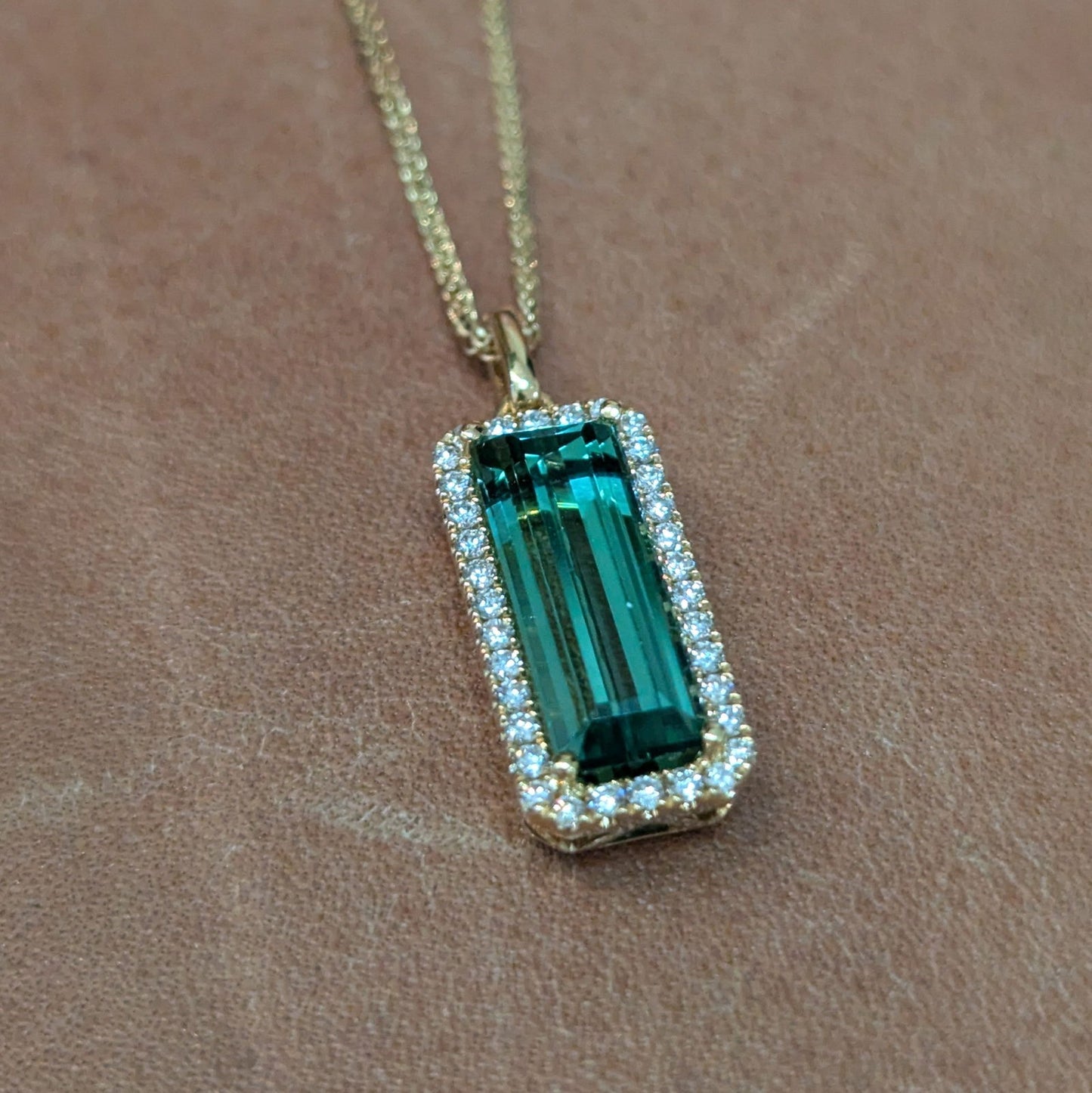 Photo of Rectangle Tourmaline Halo Pendant in a decorative scene, designed by , available at Plumb Gold & Plumb Silver