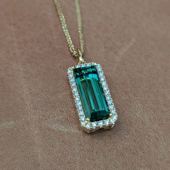 Photo of Rectangle Tourmaline Halo Pendant in a decorative scene, designed by , available at Plumb Gold & Plumb Silver