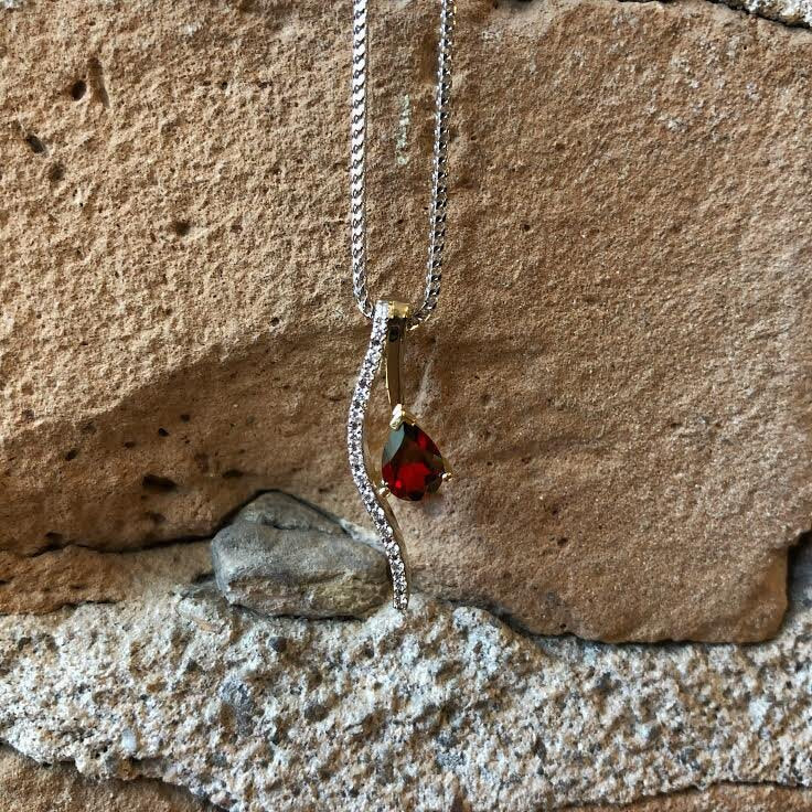 Photo of Red Garnet Swoop Pendant in a decorative scene, designed by , available at Plumb Gold & Plumb Silver