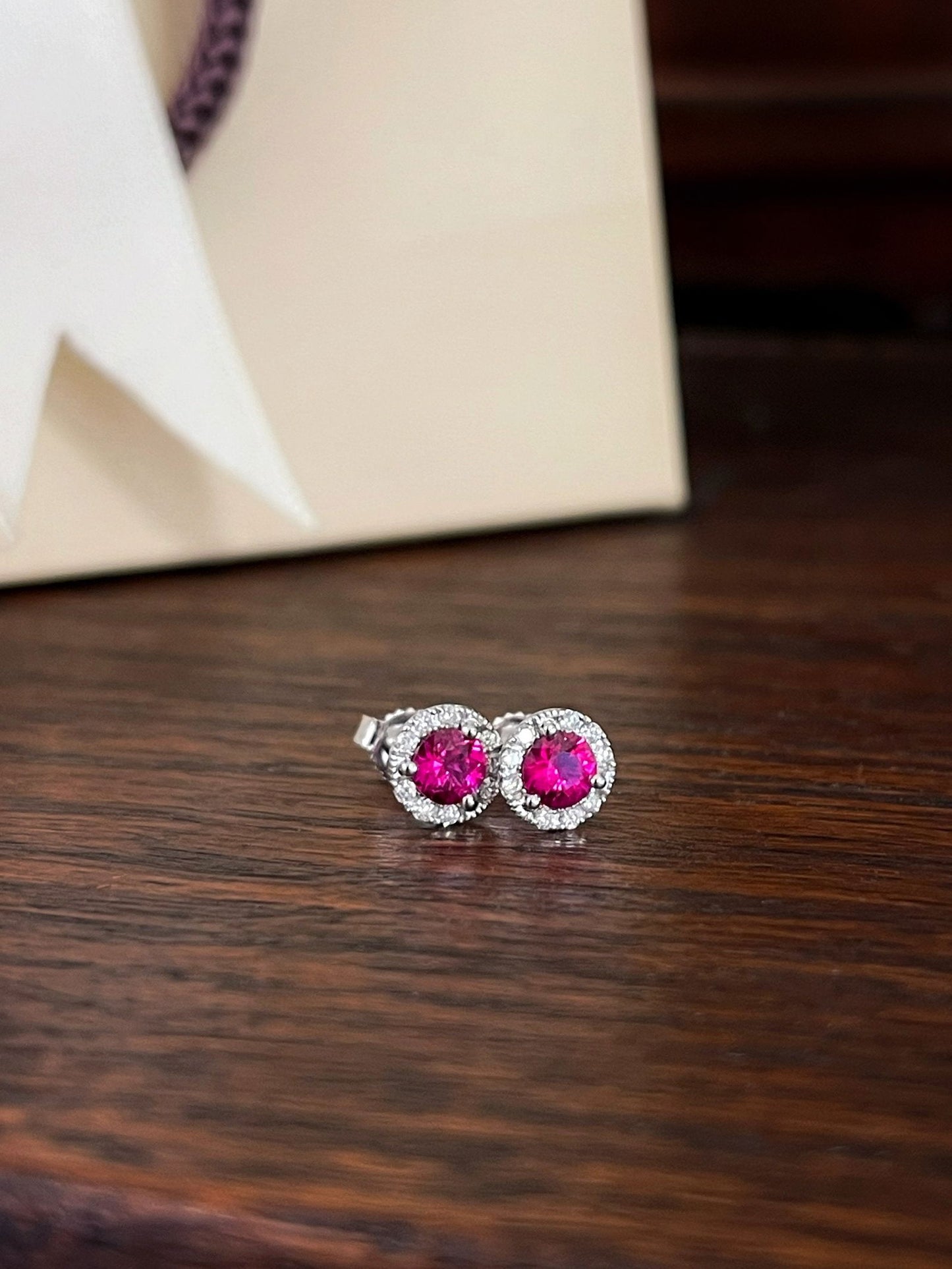 Photo of Ruby and Diamond Halo Studs in a decorative scene, designed by , available at Plumb Gold & Plumb Silver