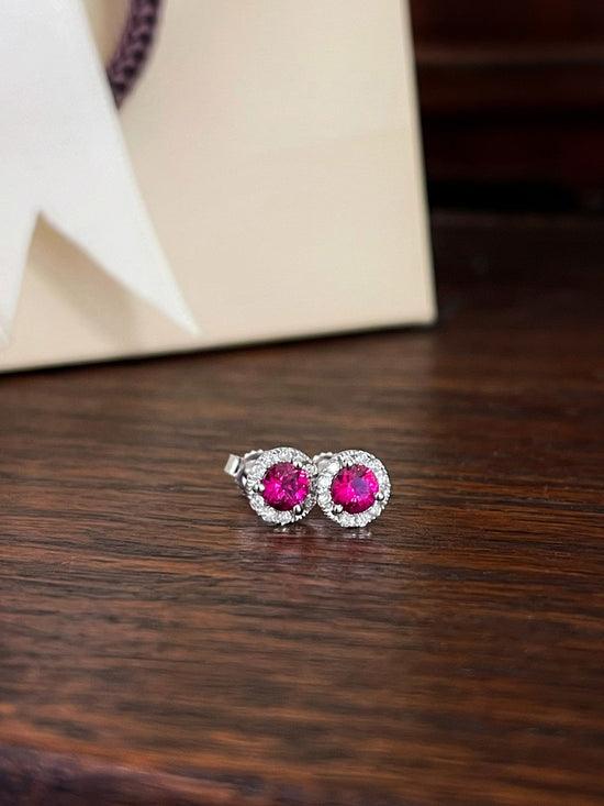 Photo of Ruby and Diamond Halo Studs in a decorative scene, designed by , available at Plumb Gold & Plumb Silver