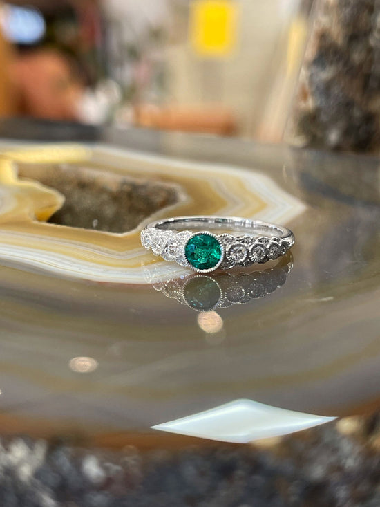 Photo of Stanton Color Emerald and Diamond Ring in a decorative scene, designed by , available at Plumb Gold & Plumb Silver