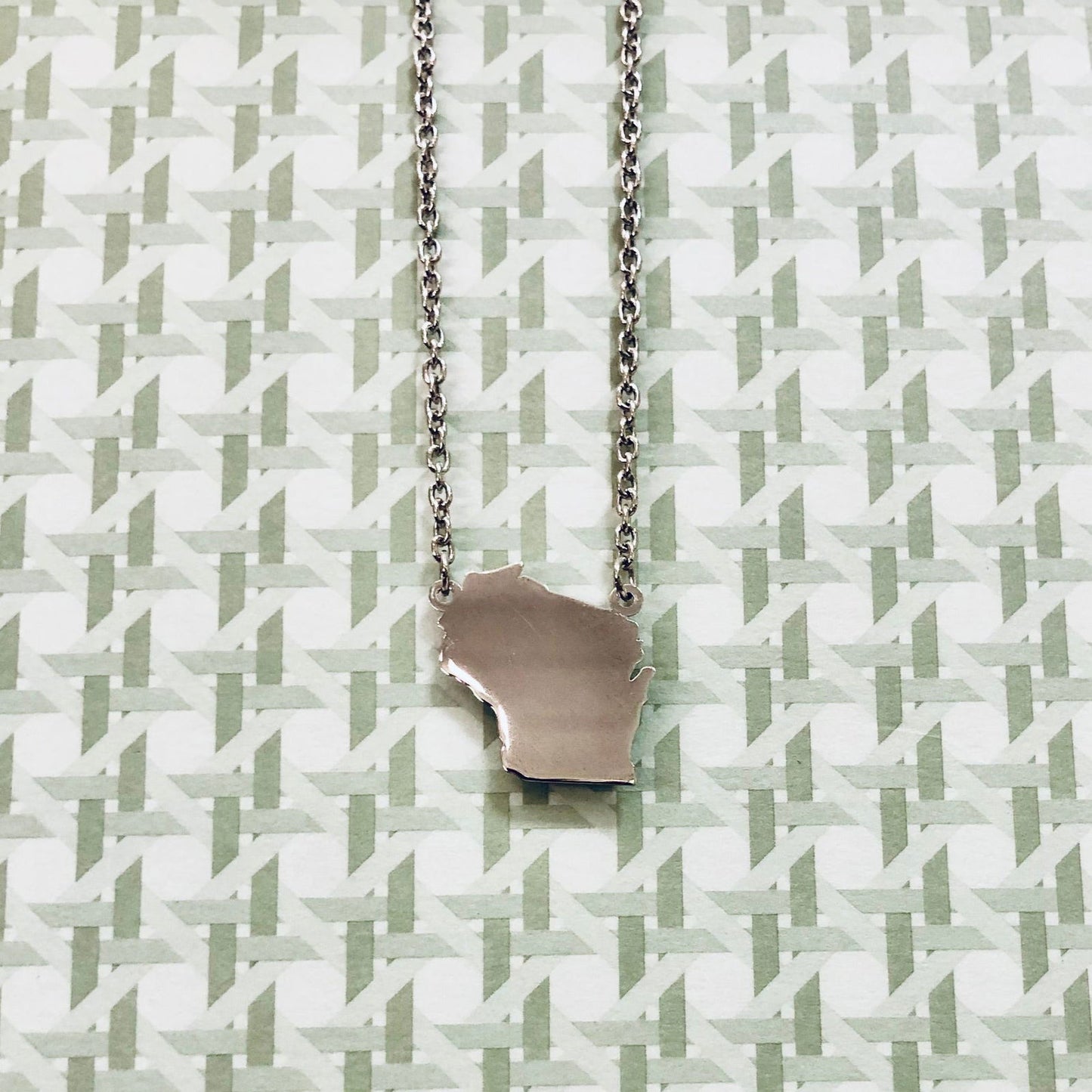 Photo of Sterling Silver Wisconsin Necklace in a decorative scene, designed by , available at Plumb Gold & Plumb Silver