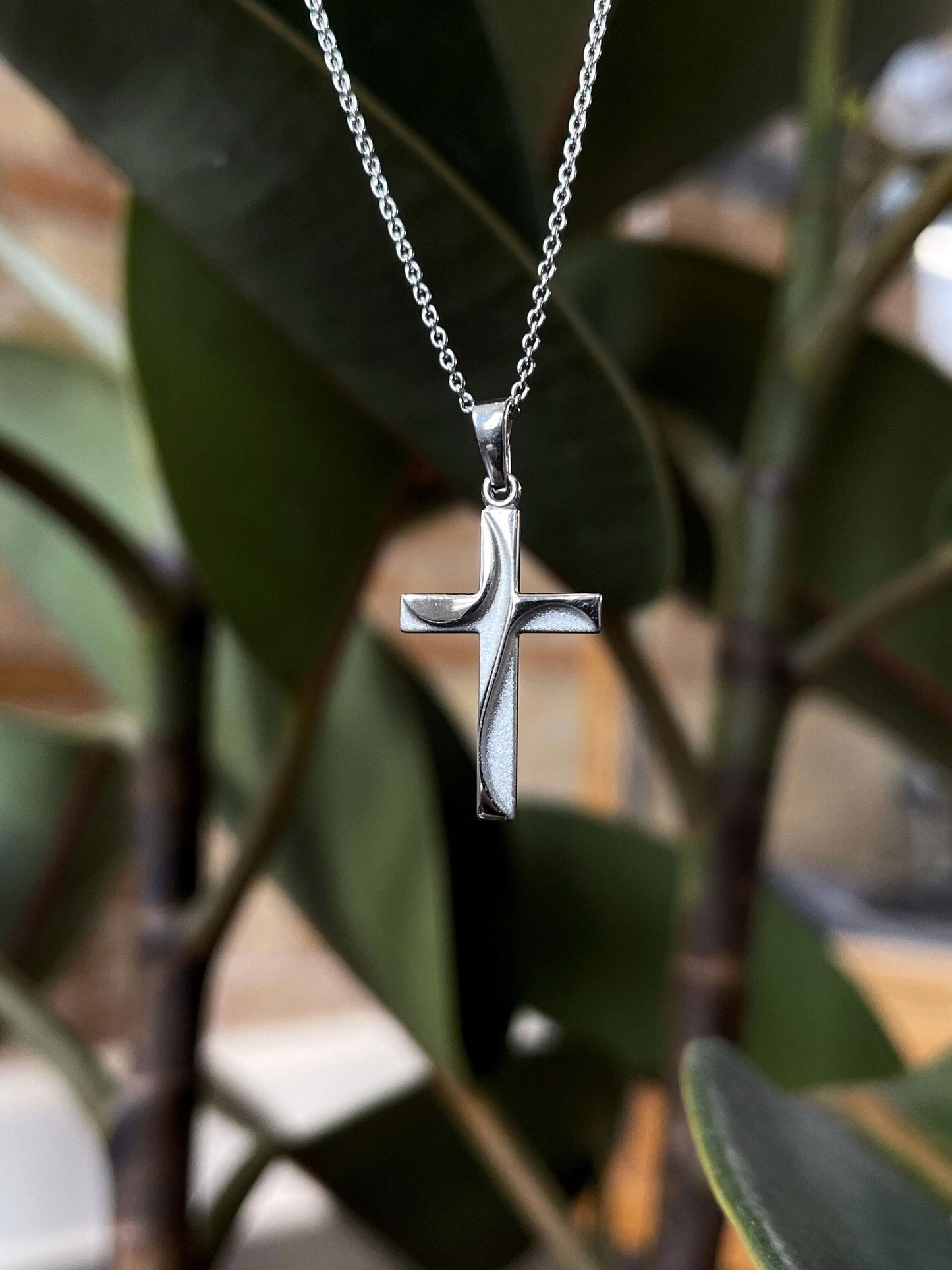 Photo of Swirl Cross Necklace in a decorative scene, designed by , available at Plumb Gold & Plumb Silver